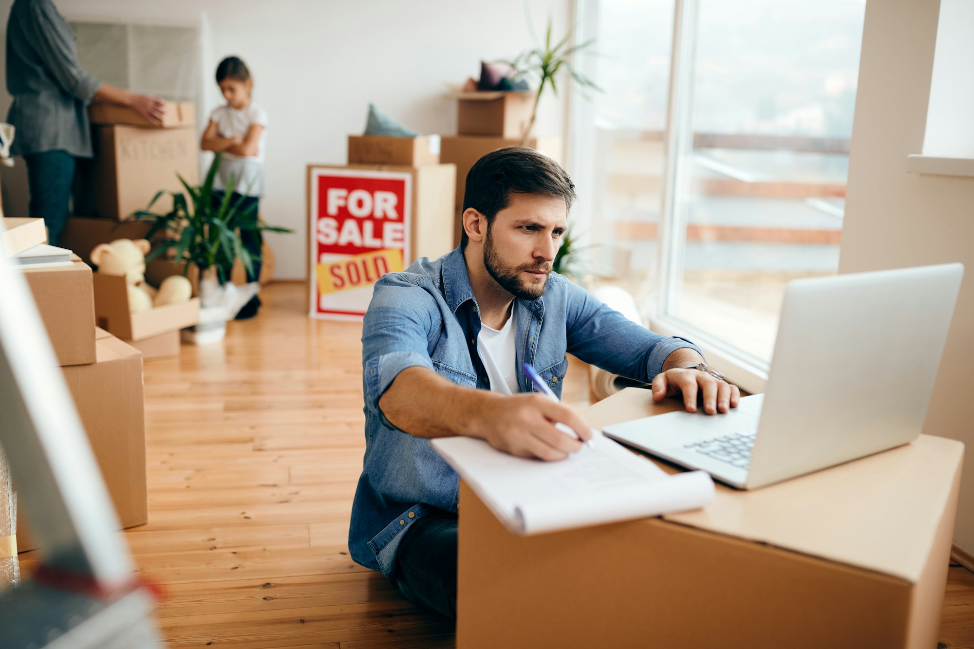 Mid adult father using laptop while filling paperwork after selling the apartment.